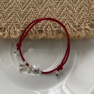 Close-up of red cord bracelet with S925 silver cat and fish pendants on a rustic surface