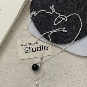 Close-up of S925 sterling silver chain with minimalist black spherical pendant on fabric