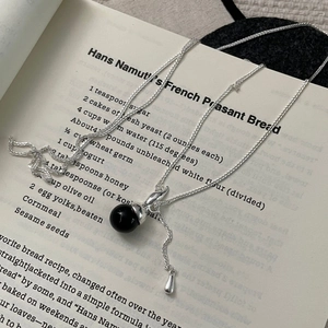 Detailed view of silver gourd necklace with a black round gemstone on vintage paper