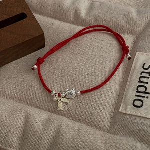Detail of red braided string bracelet with silver cat and fish charms on wood