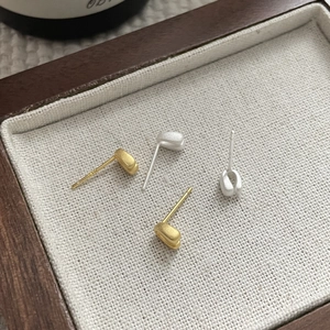 Macro view of gold and silver S925 stud earrings with a matte brushed finish on linen