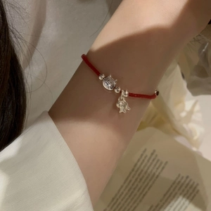 Detail of red woven rope bracelet with S925 silver cat and fish charms on woman's wrist