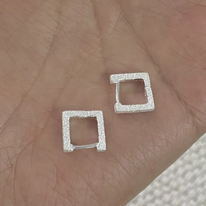 Dettaglio di orecchini quadrati in argento con finitura satinata brillante sulla mano
