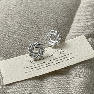 Detail shot of silver knot earrings with polished metal texture on beige fabric background