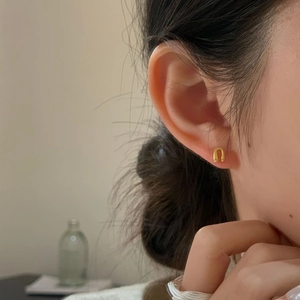 Detail view of minimalist U-shaped matte gold stud earrings worn on female earlobe