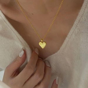 Detail of a minimalist gold heart pendant necklace worn on a cream sweater