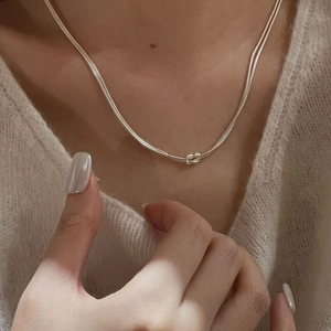 Detail of a double-layered silver snake chain necklace with knot design on collarbone