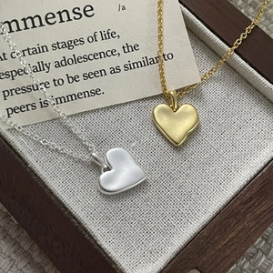 Close-up of gold and silver heart necklaces in a wooden jewelry box with a card