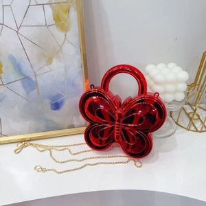 Detail of red butterfly-shaped handbag with metallic mirror finish and golden chain