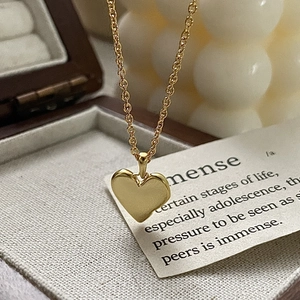 Detail of a golden heart pendant necklace resting in a jewelry box with a candle