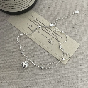 Detail of S925 sterling silver double-layer bracelet with heart pendant on linen texture