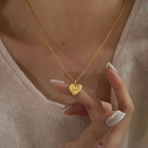 Close-up of minimalist gold heart pendant necklace worn on a cozy beige knit sweater