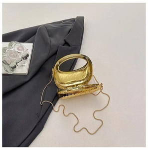 Détail d'un sac de soirée structuré en métal doré avec poignée ovale sur un blazer gris