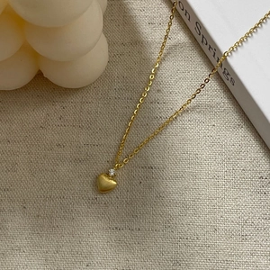 Dettaglio della collana con cuore dorato opaco e zircone su tessuto bianco morbido