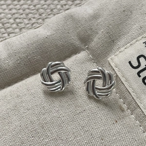 Macro shot of 925 sterling silver multi-strand woven knot stud earrings on linen texture