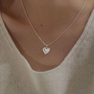 Close-up of minimalist S925 sterling silver heart pendant necklace on white knitwear