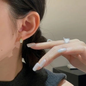 Close-up of gold shell huggie earrings and silver multi-layer coiled ring on a model