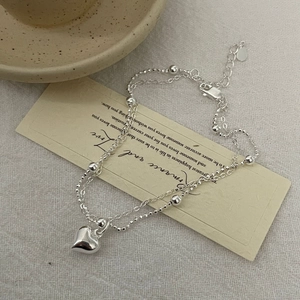 Detail view of silver double-layer heart bracelet with bead chains on elegant card
