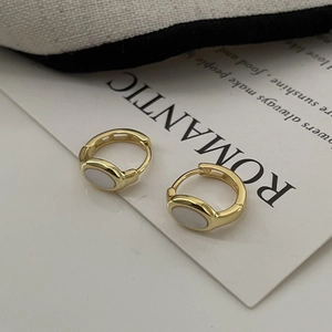 Detailed close-up of golden oval shell earrings with warm white texture and hoop design