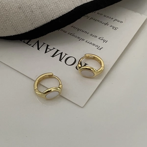 Detail of gold huggie earrings with white oval shell inlay on a romantic jewelry card
