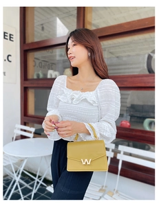 Outdoor shot of ginger yellow PU leather bag with golden W buckle on white bubble sleeve top