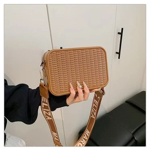 Detalle de un neceser de maquillaje trenzado marrón con correa ancha estampada