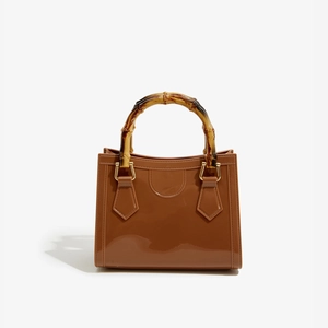 Detailed macro view of the bamboo style handle and glossy brown PVC texture on the handbag