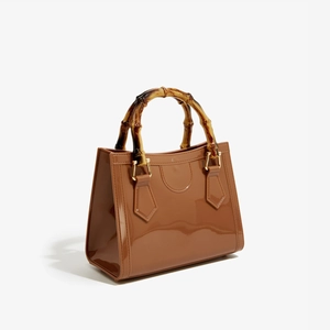 Detailed view of brown glossy PVC handbag featuring authentic bamboo handle and gold hardware