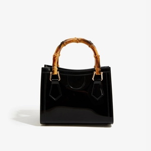 Close-up of glossy black PVC square bag featuring authentic bamboo top handles and gold hardware