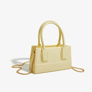 Detail of creamy yellow PVC jelly bag with golden chain strap and cylindrical handle