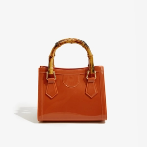Close-up of orange PVC bag featuring high-gloss finish and natural bamboo handle detail