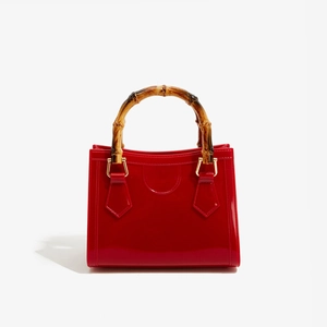 Macro shot of red glossy jelly bag featuring vintage bamboo handle and gold hardware