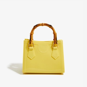 Detail of a yellow jelly tote bag featuring a bamboo top handle with gold metal connectors