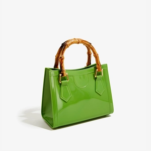 Detailed view of glossy green PVC handbag featuring a natural bamboo handle and gold hardware