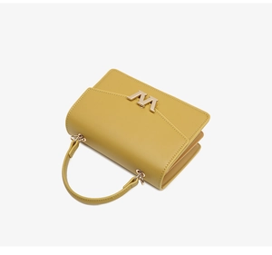 Detail view of bright yellow leather handbag featuring a golden M magnetic buckle