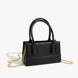 Detail view of black square PVC bag with golden chain strap and polished leather texture