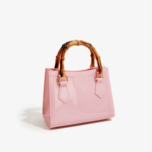 Pink PVC jelly tote bag with bamboo top handles and gold metal connectors on white background