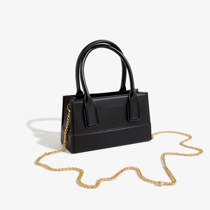 Detail view of black rectangular handbag featuring gold chain strap and smooth leather texture