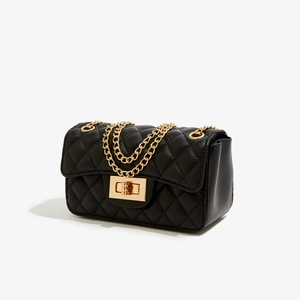 Detail of black quilted leather shoulder bag with gold chain strap and metal clasp