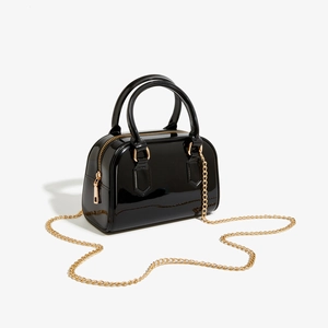 Détail du sac à main en PVC noir brillant avec bandoulière en chaîne dorée et fini poli