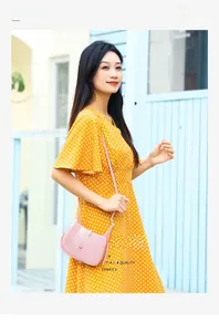 Outdoor shot of a chic pink PVC crescent crossbody bag paired with a yellow dress