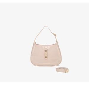 Detail of beige crescent PVC jelly bag showing glossy texture and gold piston clasp hardware