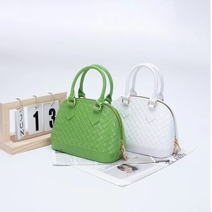 Close-up of woven shell bags in green and white with gold zipper and dual handles