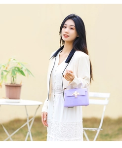 Détail du sac gelée en PVC lilas avec fermoir fleur de lys doré sur robe blanche