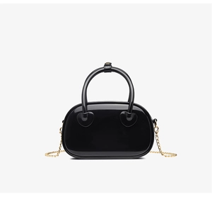 Detail of glossy black PVC bag featuring heart shaped handle base and gold chain strap