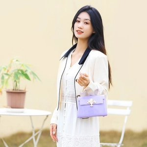 Mini sac à main en PVC violet avec fermoir floral doré porté par un mannequin dehors