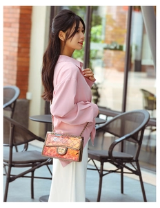 Detailed close-up of a holographic quilted PVC chain bag worn by a model in a café