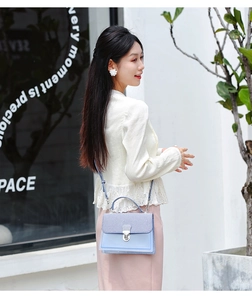 Detail shot of light blue minimalist crossbody bag featuring silver buckle and textured flap