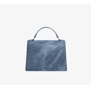 Detalle de un bolso trapecio de PVC con textura de denim azul y herrajes plateados