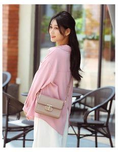 Chic beige crossbody bag with gold buckle worn by a model in a cafe setting